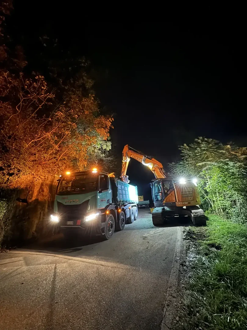 Lavori stradali notturni con escavatore e camion operativi su carreggiata